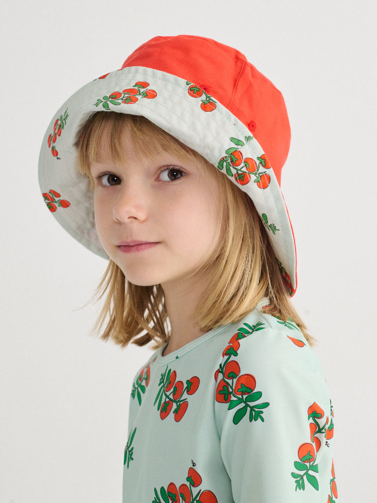 Child wearing a red and white hat with cherry pattern, matching shirt with cherry pattern on a light gray background